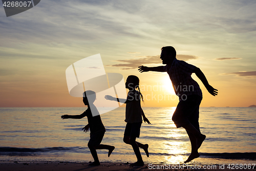 Image of Father and children playing on the beach at the sunset time.