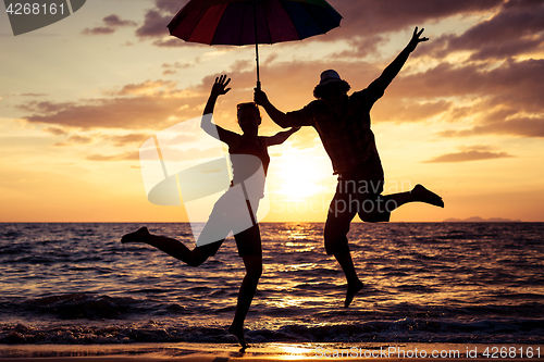 Image of Happy family jumping on the beach at the sunset time.