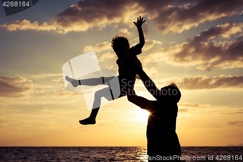 Image of Father and son playing on the beach at the sunset time.
