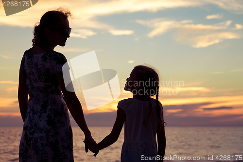 Image of Mother and daughter playing on the beach at the sunset time.