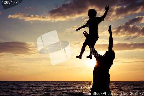 Image of Father and son playing on the beach at the sunset time.