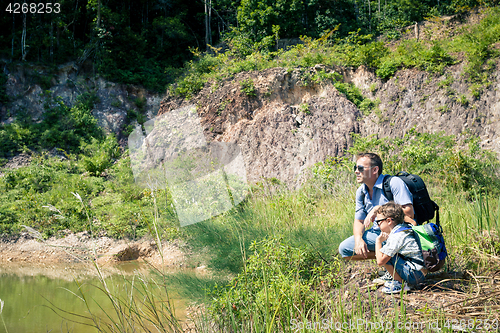 Image of Father and son siting near the pond at the day time.