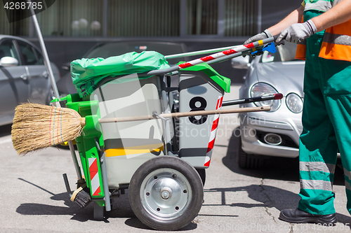 Image of Worker of cleaning company in green uniform with garbage bin.