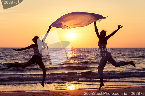 Image of Mother and daughter jumping on the beach at the sunset time. 