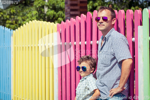 Image of Father and son standing near the multicolored fence at the day t