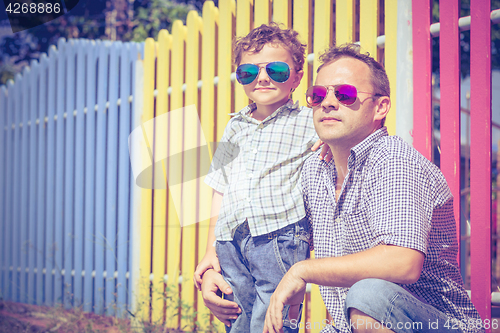 Image of Father and son standing near the multicolored fence at the day t