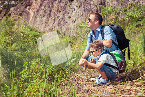 Image of Father and son siting near the pond at the day time.