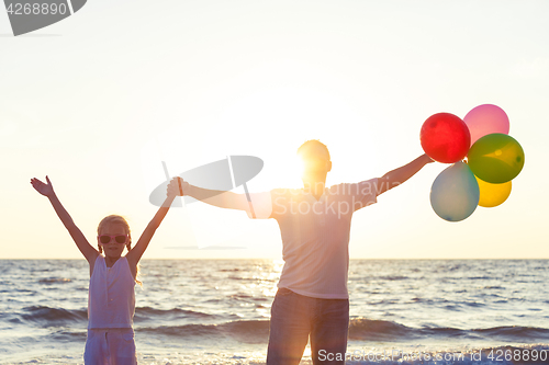 Image of Father and daughter with balloons playing on the beach at the su