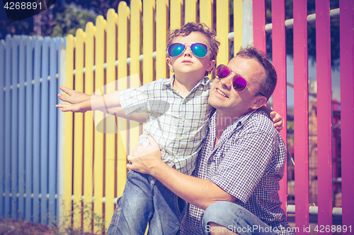 Image of Father and son standing near the multicolored fence at the day t