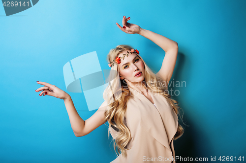 Image of young pretty blond girl with curly blond hair and little lowers happy smiling on blue sky background