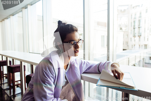 Image of young cute hipster girl student sitting in cafe with notebook reading, wearing glasses, lifestyle happy smiling people concept