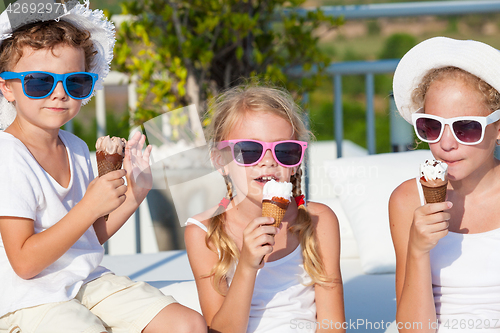 Image of three happy children eating ice cream near swimming pool at the 