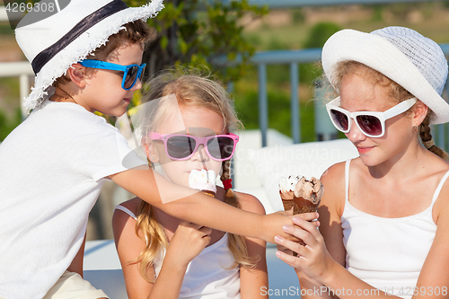 Image of three happy children eating ice cream near swimming pool at the 