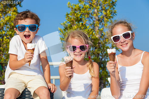 Image of three happy children eating ice cream near swimming pool at the 