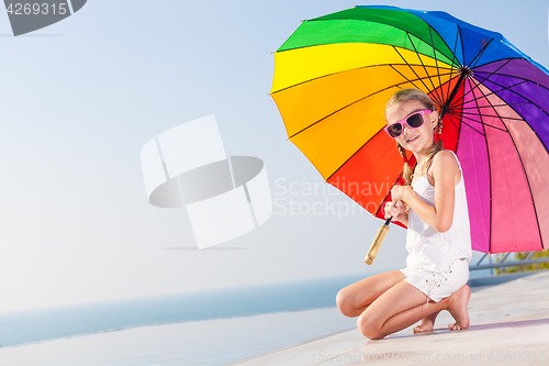 Image of happy little girl with umbrella sitting near a swimming pool