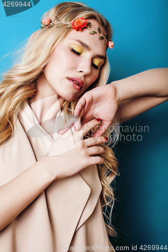 Image of young pretty blond girl with curly blond hair and little lowers happy smiling on blue sky background, lifestyle people concept