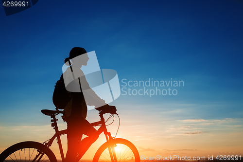 Image of Silhouette of cyclist and a bike on sky background