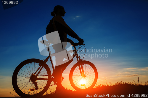 Image of Silhouette of cyclist and a bike on sky background