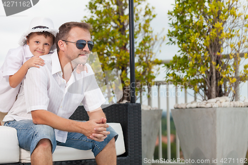 Image of Father and son relaxing near a swimming pool  at the day time.