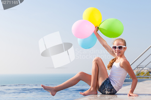 Image of happy teen girl with balloons sitting near a swimming pool