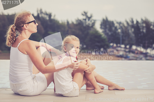 Image of Mother and daughter relaxing near a swimming pool  at the day ti