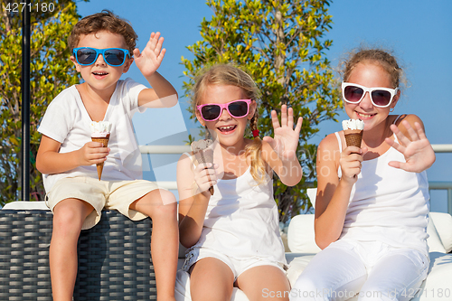 Image of three happy children eating ice cream near swimming pool at the 