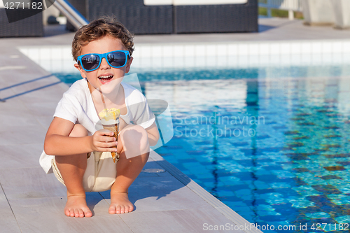 Image of happy little boy with ice cream  sitting near a swimming pool