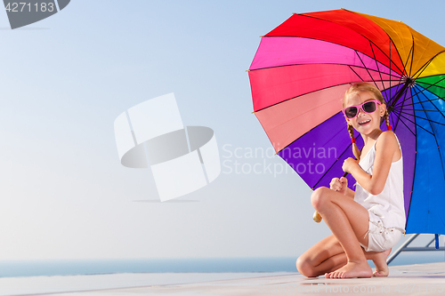 Image of happy little girl with umbrella sitting near a swimming pool