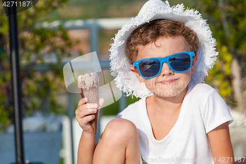 Image of happy little boy with ice cream  sitting near a swimming pool