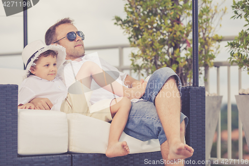 Image of Father and son relaxing near a swimming pool  at the day time.