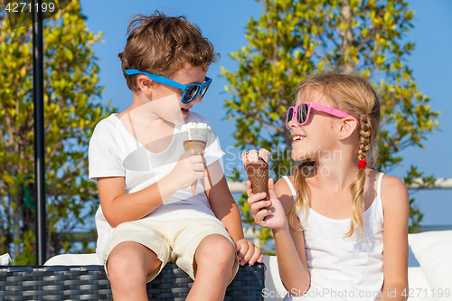 Image of Two happy children eating ice cream near swimming pool at the da