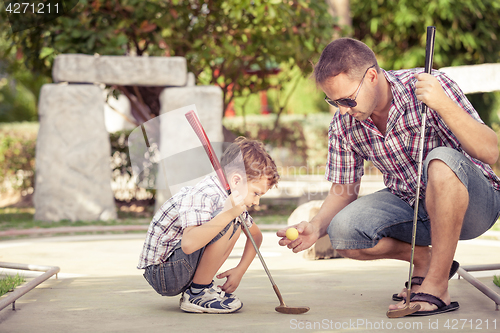 Image of Cheerful young man teaching his son to play mini golf at the day