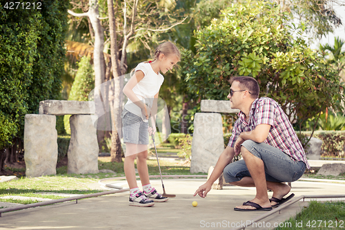 Image of Cheerful young man teaching his daughter to play mini golf at th