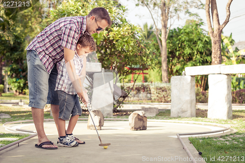 Image of Cheerful young man teaching his son to play mini golf at the day