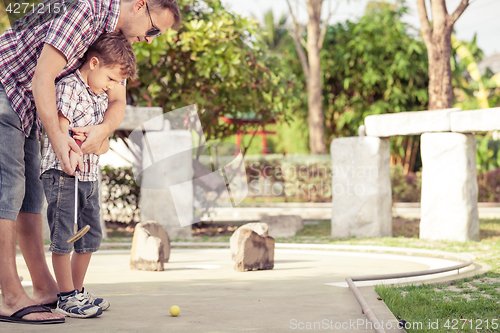 Image of Cheerful young man teaching his son to play mini golf at the day