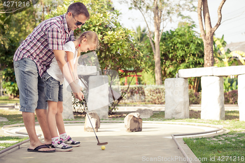 Image of Cheerful young man teaching his daughter to play mini golf at th