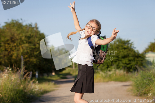 Image of Smiling young school girl in a school uniform jumping on the roa