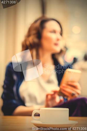 Image of cup of tea on the table and a woman with a smartphone in the blu