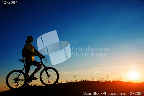 Image of Silhouette of cyclist and a bike on sky background