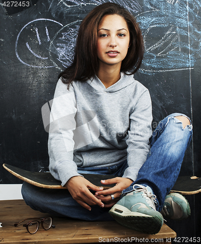 Image of young cute teenage girl in classroom at blackboard seating on ta