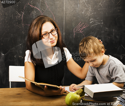 Image of little cute boy with young teacher in classroom studying at blac