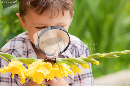 Image of Happy little boy playing in the park with snail at the day time.