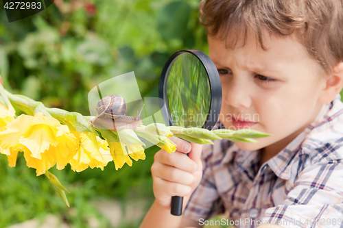 Image of Happy little boy playing in the park with snail at the day time.