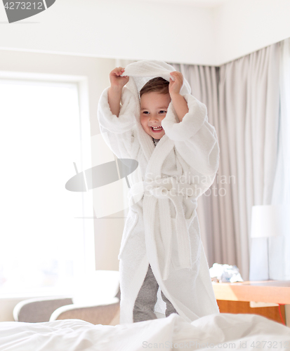 Image of happy little boy in bathrobe on home or hotel bed