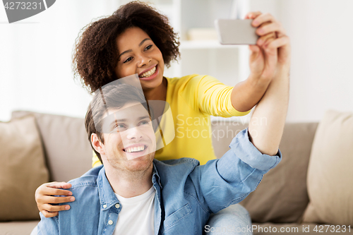 Image of happy couple with smartphone taking selfie at home