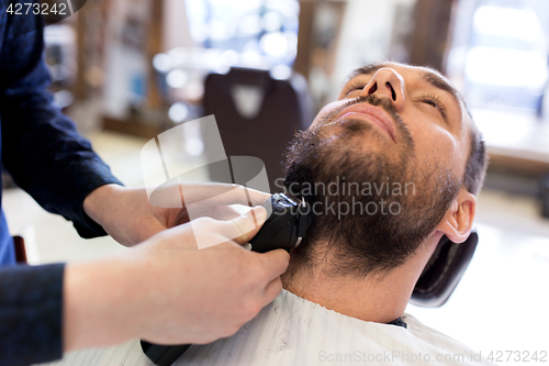 Image of man and barber with trimmer cutting beard at salon