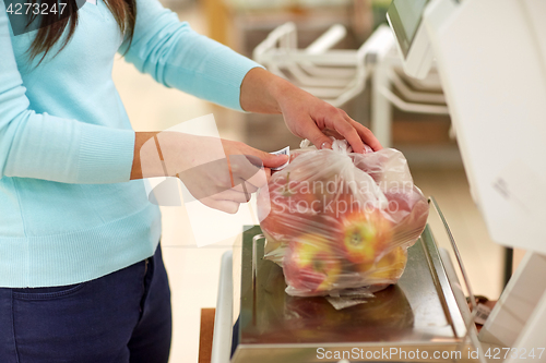 Image of woman weighing apples on scale at grocery store