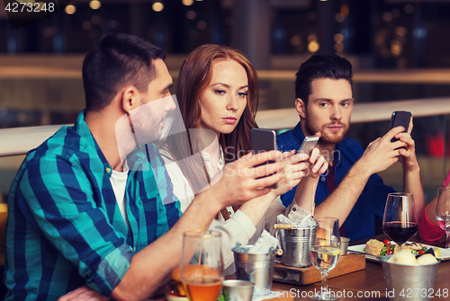 Image of friends with smartphones dining at restaurant