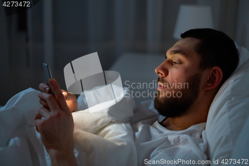 Image of man with smartphone in bed at night