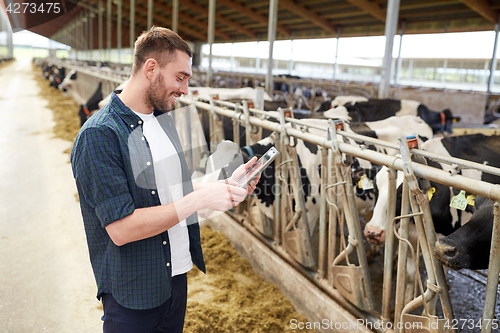 Image of young man with tablet pc and cows on dairy farm